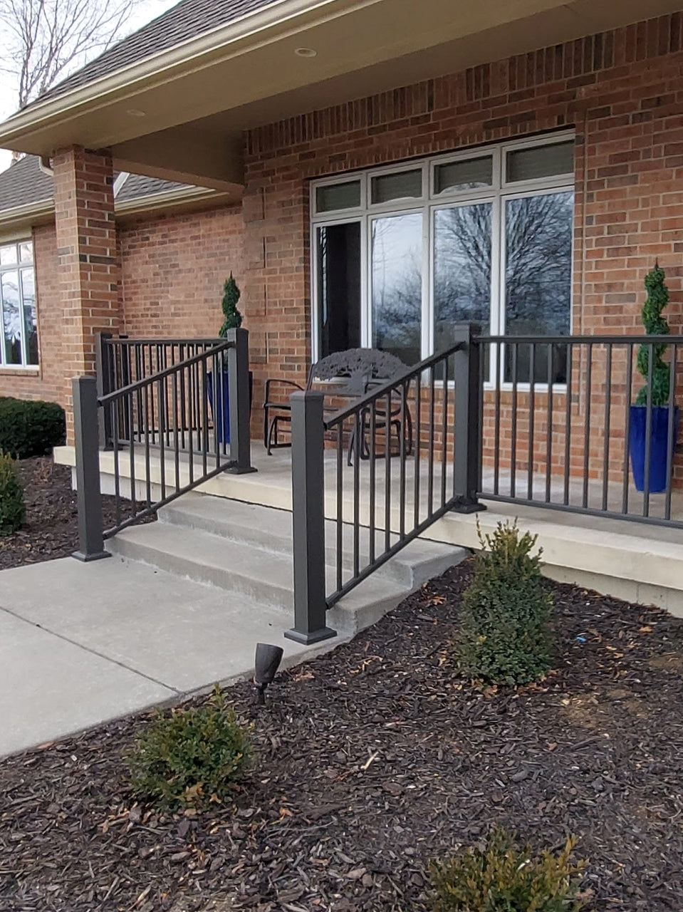 Aluminum railing like dekpro prestige in cocoa bronze infront of a house on concrete is the best option for patio railing because it can attach to the top of concrete pad for sturdy front porch railing